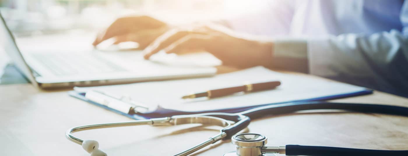 Doctor typing information on Laptop in Hospital office focus on Stethoscope